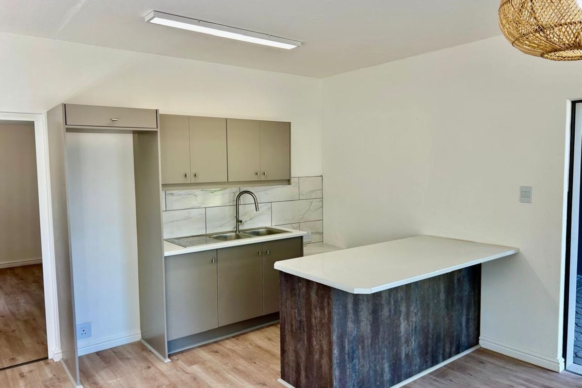 A modern kitchen featuring neutral cabinetry, a stone-look breakfast bar, marble-effect tiled splashback, and light wood-look flooring.
