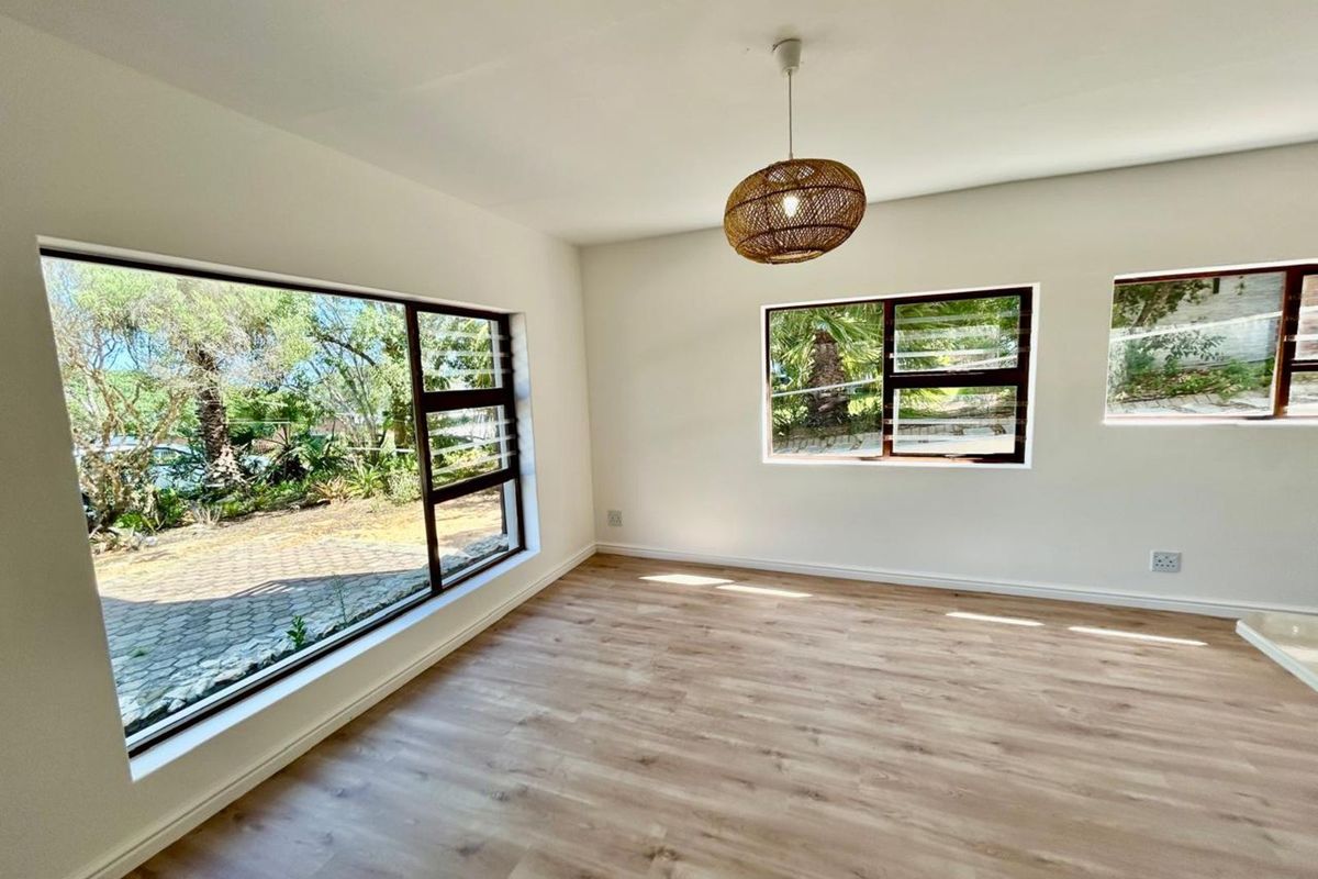 A bright, empty bedroom featuring modern wood-look laminate flooring, large windows with garden views, and a contemporary pendant light fixture.