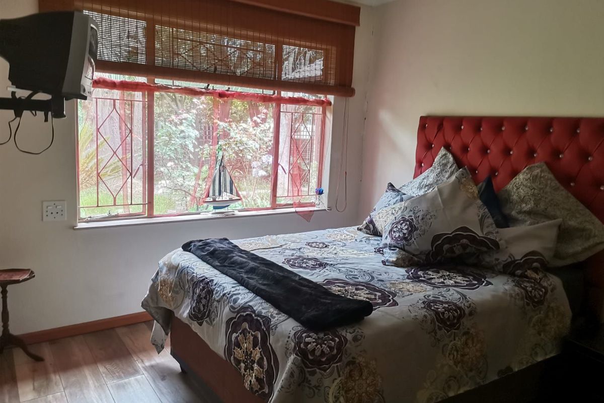 A bedroom featuring wood-look flooring, a large window with security bars, and a bamboo roller blind.