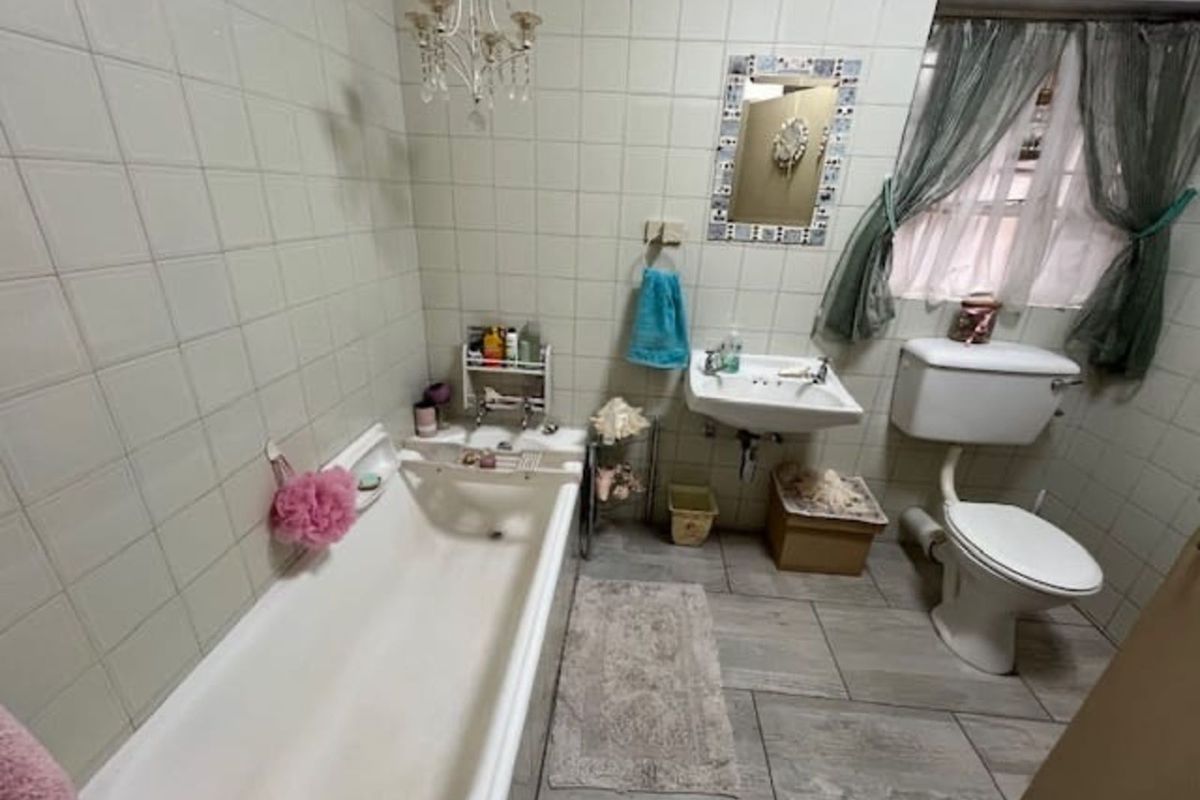 A functional bathroom featuring a standard bathtub, wall-mounted basin, and toilet with neutral wall tiling and modern grey floor tiles.
