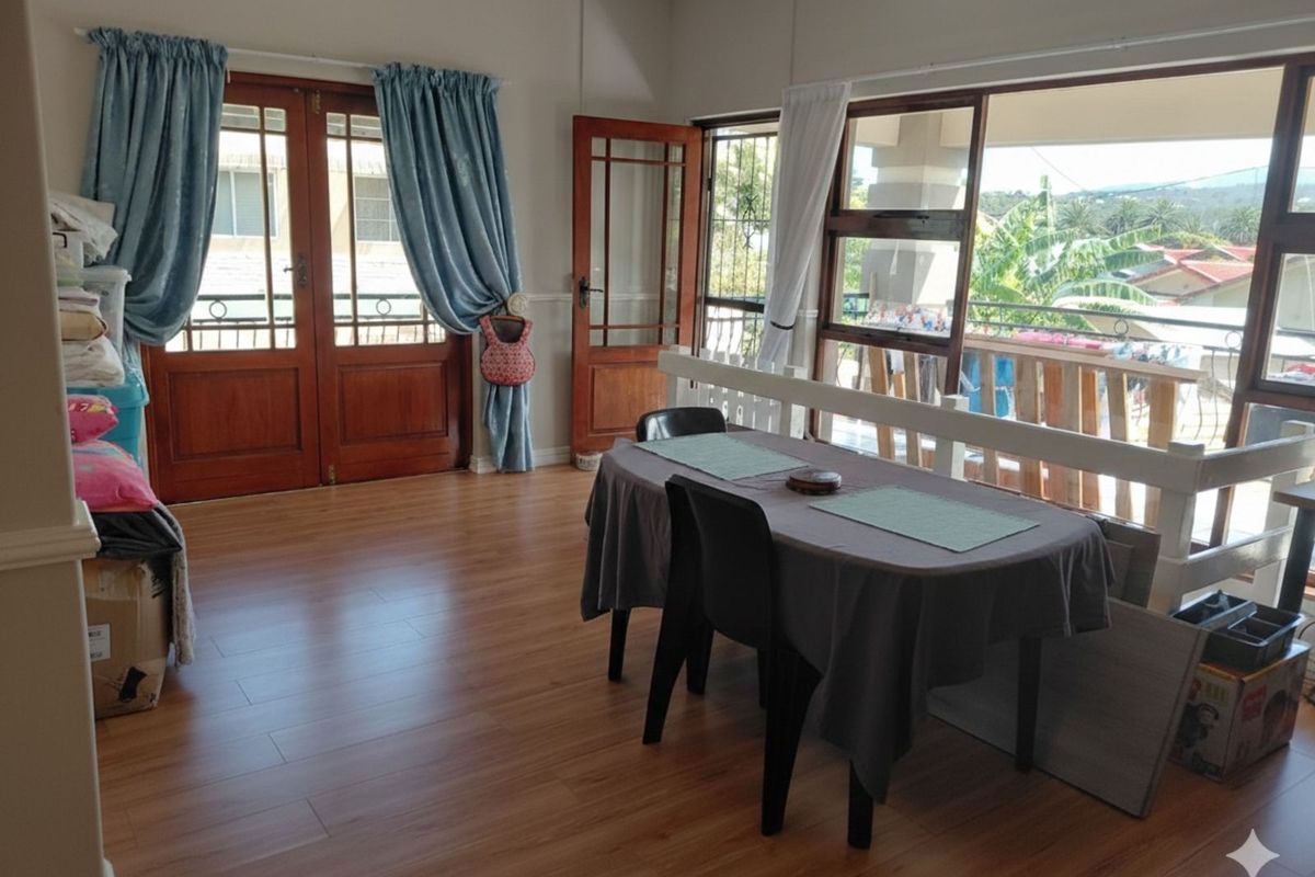 Bright living area featuring wood-look laminate flooring, timber-framed glass doors, and large windows providing access to an outdoor balcony space.