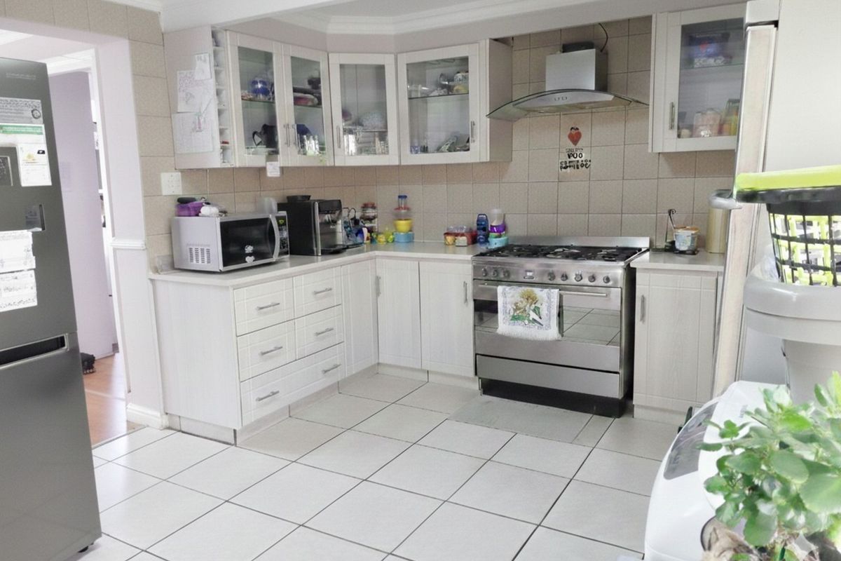 A functional kitchen featuring white cabinetry, tiled splashbacks, a stainless steel gas stove with extractor fan, and tiled flooring.
