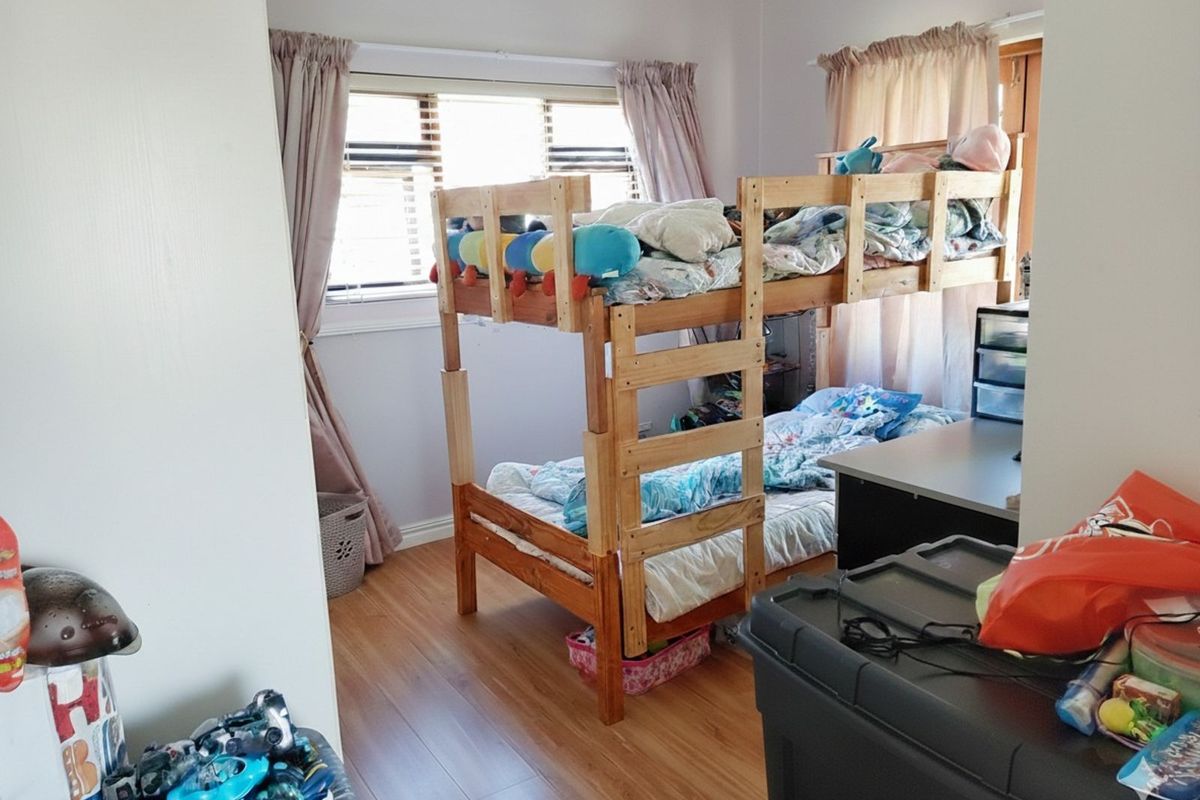 A bedroom featuring laminate flooring and large windows, providing natural light and a functional layout for a child's room.
