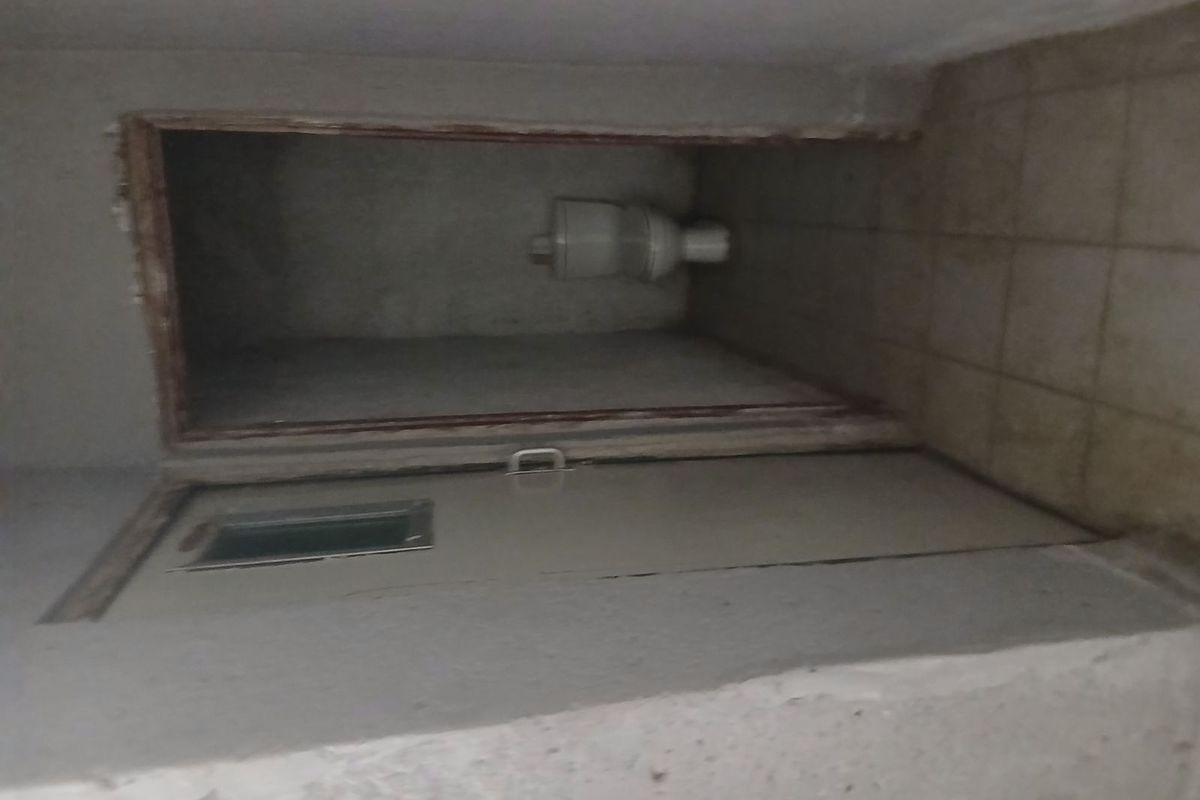 A small, utilitarian restroom space featuring basic toilet infrastructure, unfinished wall surfaces, and tiled flooring in need of renovation.