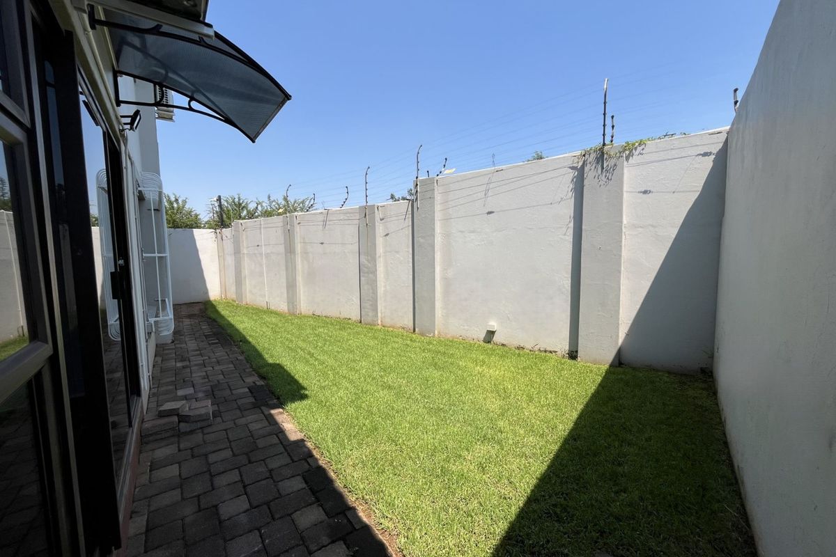 A private rear garden featuring a paved walkway, well-maintained lawn, and high perimeter walls equipped with electric fencing for added security.