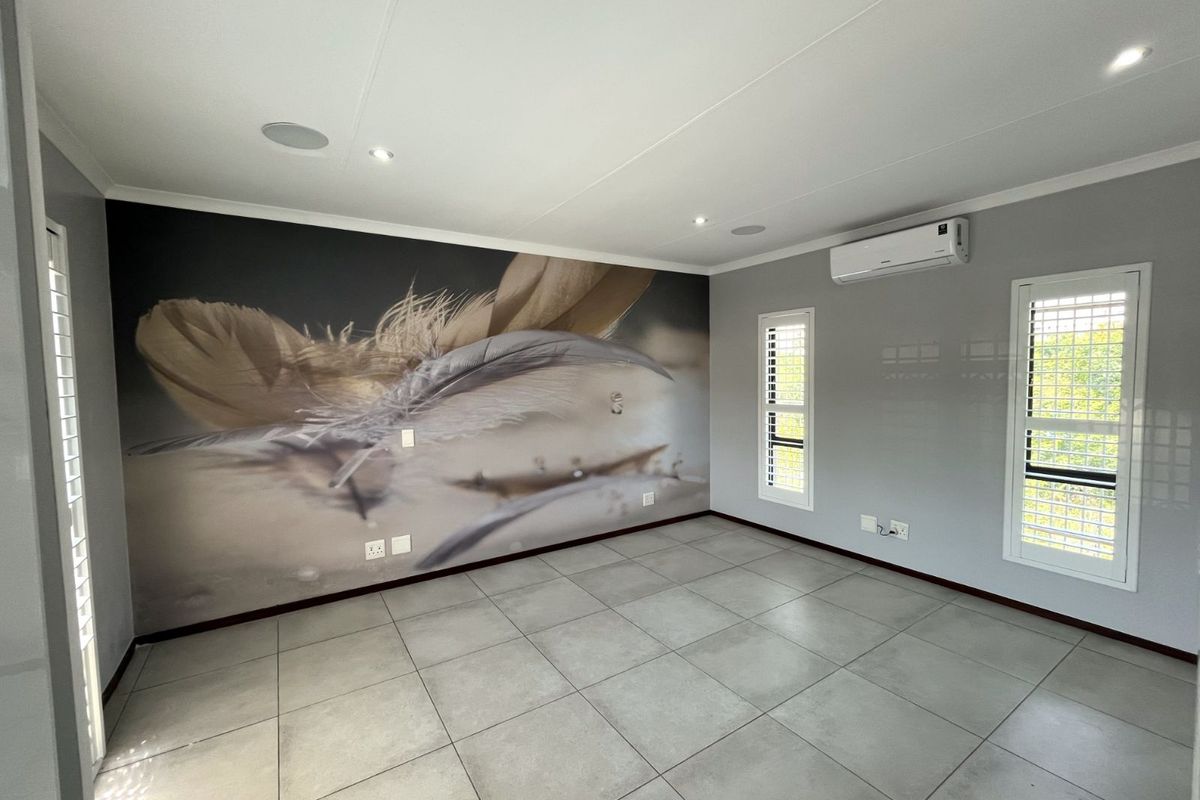 A bright, empty bedroom featuring large format floor tiles, a feature wall with mural, recessed ceiling lighting, and a wall-mounted air conditioning unit.