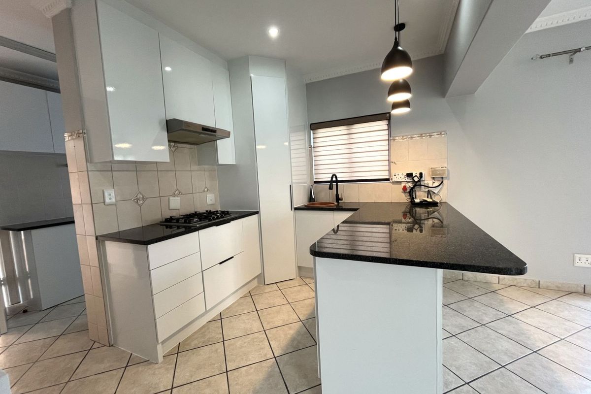 Modern kitchen featuring white cabinetry, black granite countertops, a gas hob, extractor fan, and a breakfast bar island with pendant lighting.
