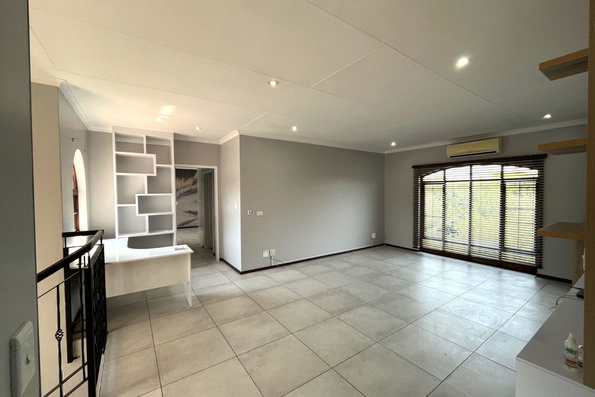 Spacious living area featuring large format floor tiles, recessed ceiling lighting, built-in shelving, and a wall-mounted air conditioning unit.