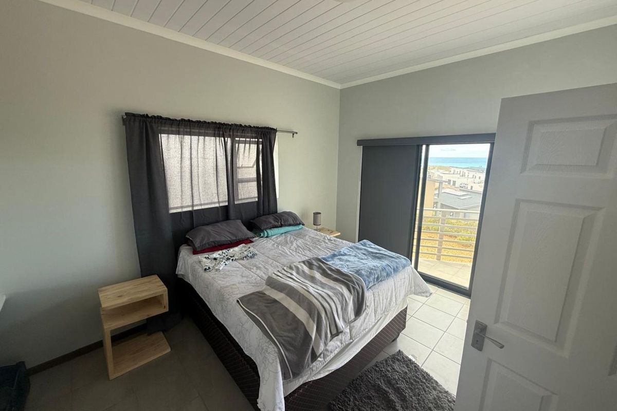 A bedroom featuring tiled flooring, a white tongue-and-groove ceiling, and a sliding glass door providing access to a balcony with coastal views.