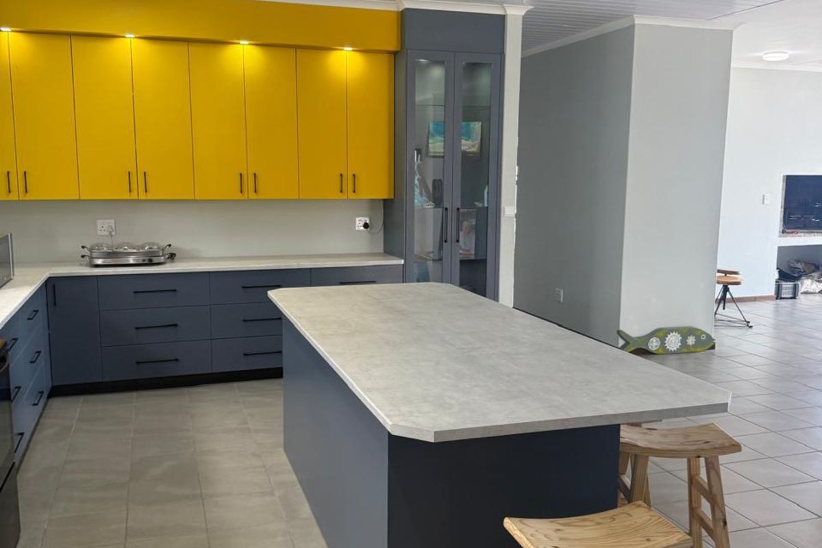 Modern kitchen featuring a central island, contrasting yellow and grey cabinetry, stone-look countertops, and tiled flooring in an open-plan layout.