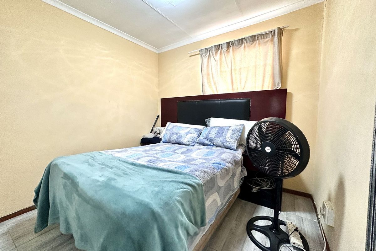 A standard bedroom featuring tiled flooring, a built-in headboard, and a window with curtain fittings.