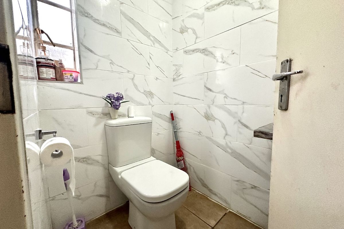 A compact guest bathroom featuring modern marble-look wall tiling, a standard toilet, and a small window for natural light.