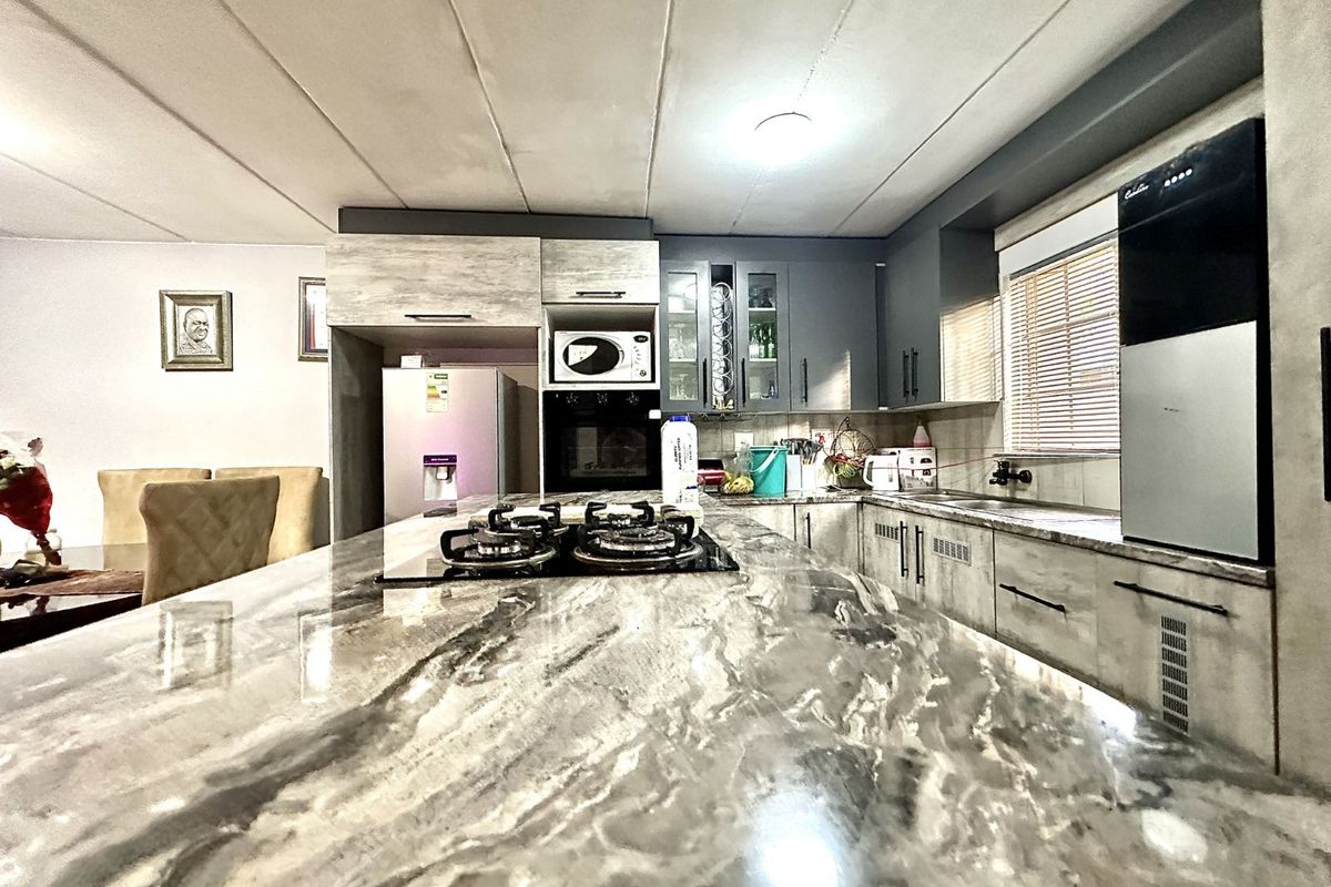 Modern kitchen featuring a large stone-topped island with integrated gas hob, ample cabinetry, and built-in oven, seamlessly flowing into the dining area.