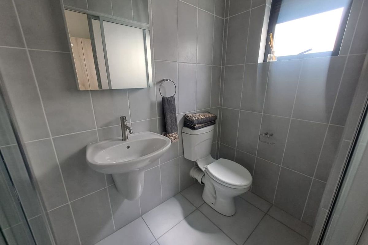 A modern bathroom featuring grey wall and floor tiles, a wall-mounted basin, a toilet, and a mirror.