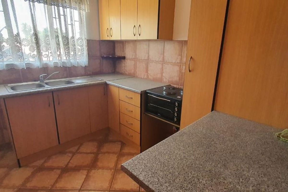 A functional kitchen featuring wood-look cabinetry, laminate countertops, a double-basin sink, and a built-in oven, finished with ceramic floor and wall tiles.