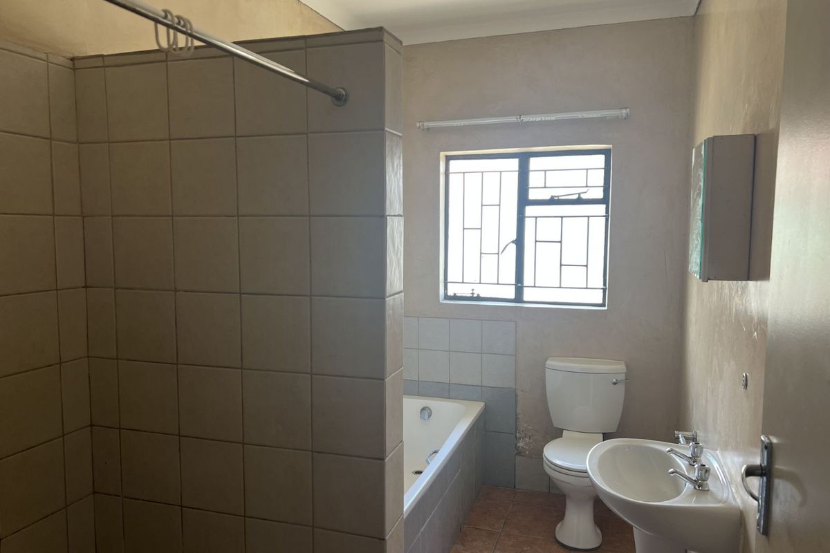 A dated bathroom featuring a tiled shower enclosure, built-in bathtub, pedestal basin, and toilet, with a window providing natural light.