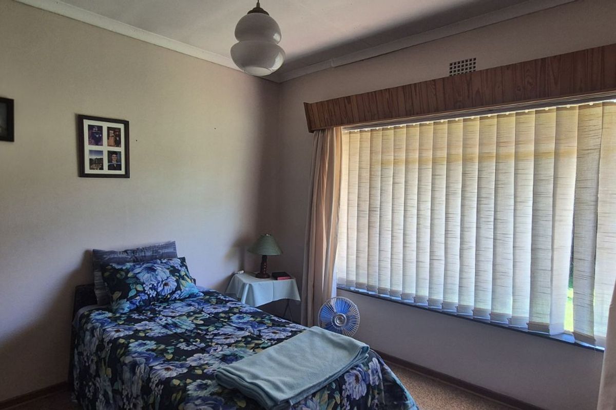 A bedroom featuring a large window with vertical blinds, a wooden pelmet, and neutral wall finishes.