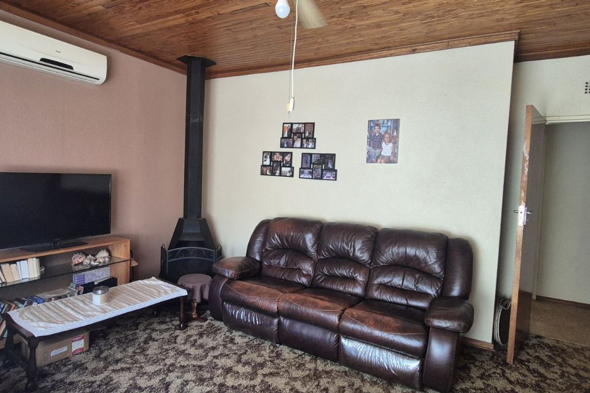 Living room featuring a wood-burning fireplace, wall-mounted air conditioning unit, and wood-paneled ceiling.