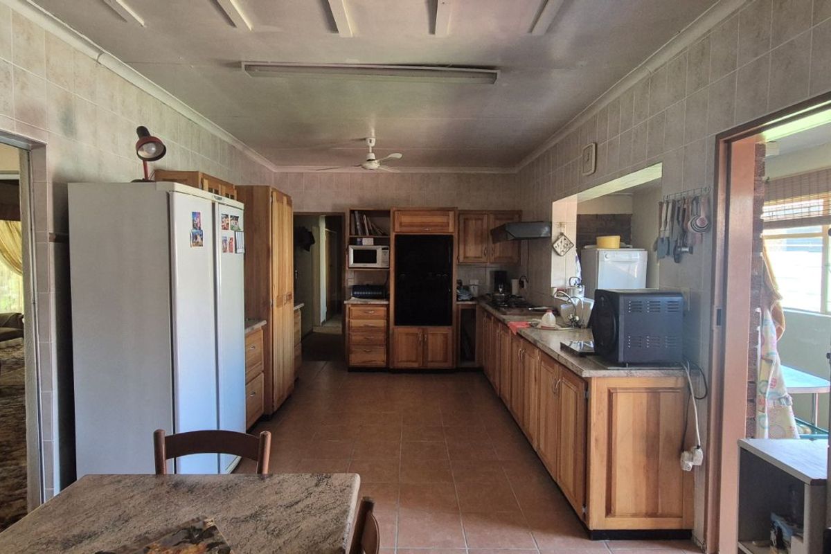 A spacious kitchen featuring wooden cabinetry, tiled flooring, and wall-to-wall tiling, offering a functional layout with ample storage and counter space.