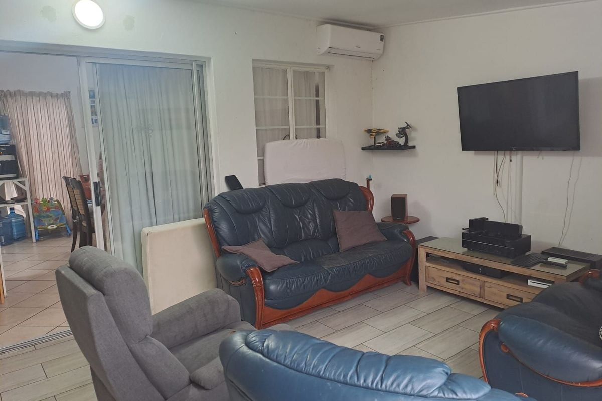 A living room featuring tiled flooring, a wall-mounted air conditioning unit, and sliding glass doors leading to an adjacent space.