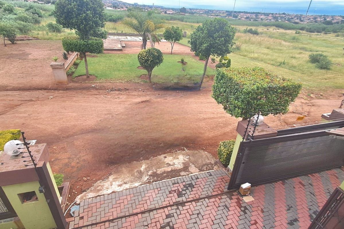 Elevated view overlooking the property grounds, featuring a paved entrance area, landscaped garden sections, and an expansive unpaved driveway.