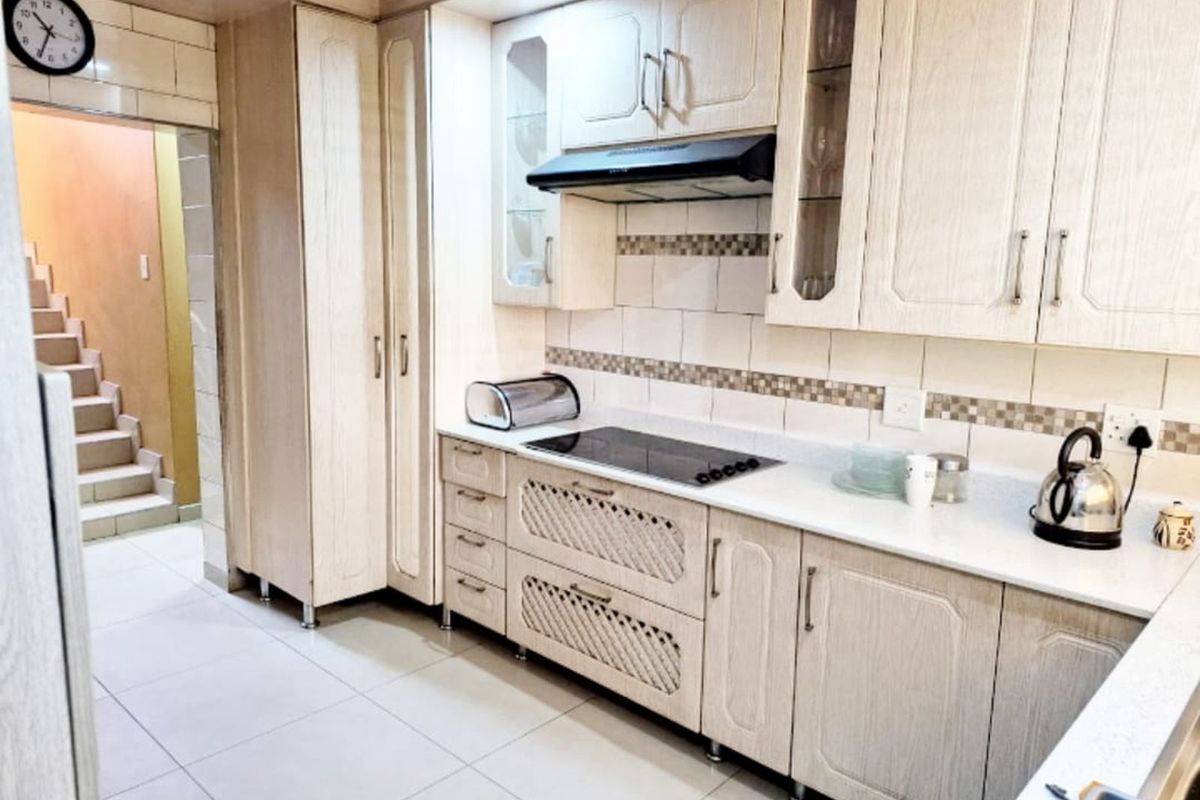 A functional kitchen featuring light-toned cabinetry, a built-in electric hob, extractor fan, and tiled flooring, with an adjacent staircase visible.