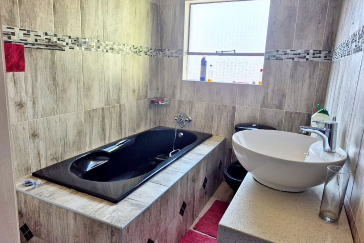 A bathroom featuring a built-in black bathtub, a modern vessel sink on a stone vanity, and floor-to-ceiling wood-look wall tiles.