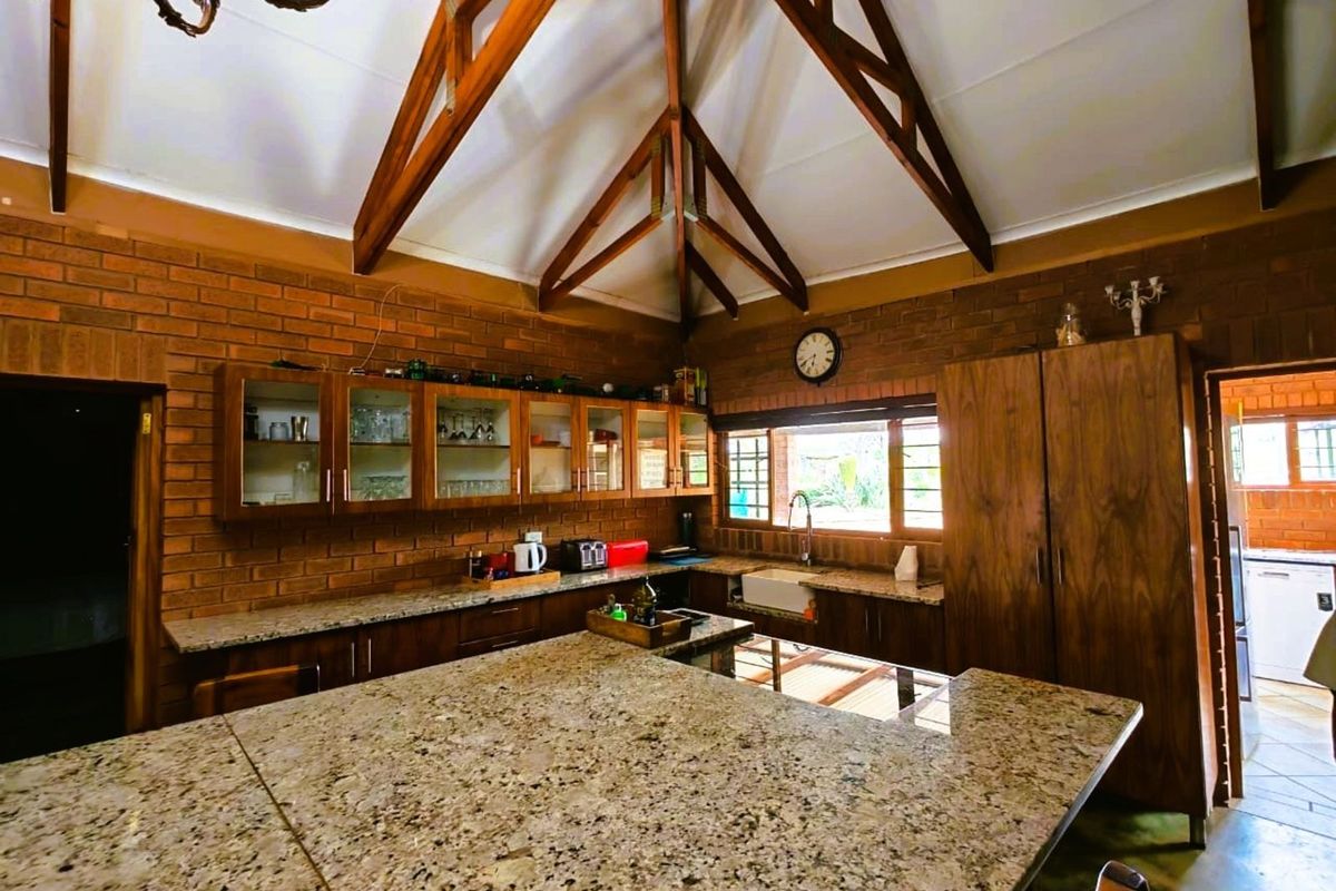 Spacious farmhouse kitchen featuring exposed timber roof trusses, granite countertops, wooden cabinetry, and a classic farmhouse sink.