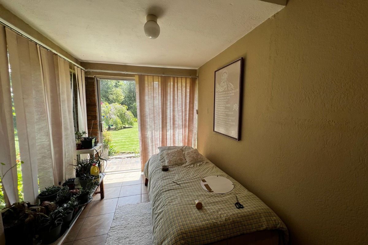 A sun-filled bedroom or multi-purpose room featuring tiled flooring and direct access to the rear garden through a sliding glass door.