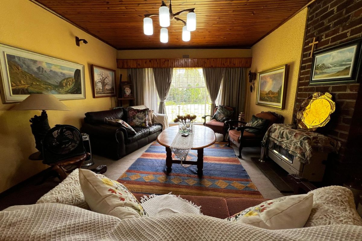 A traditional living room featuring a brick fireplace, timber-paneled ceiling, and large window providing natural light.