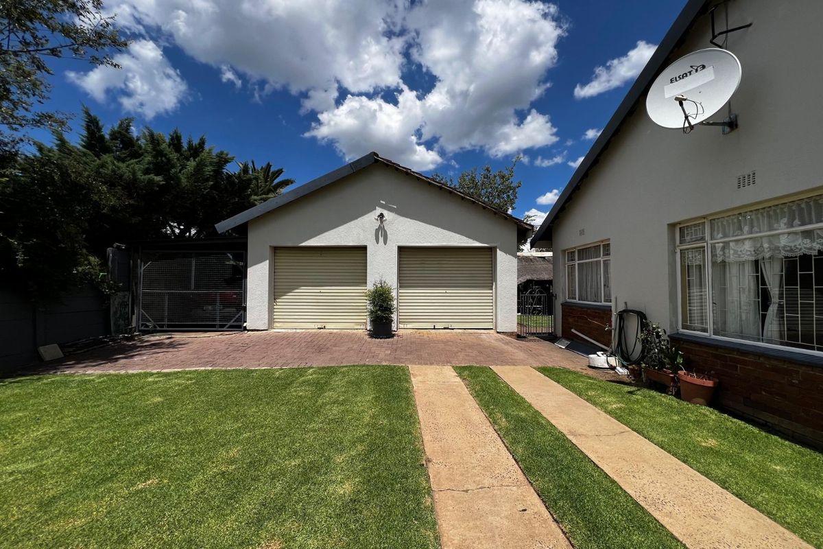A view of the rear exterior featuring a double garage, paved driveway, and a well-maintained lawn area.