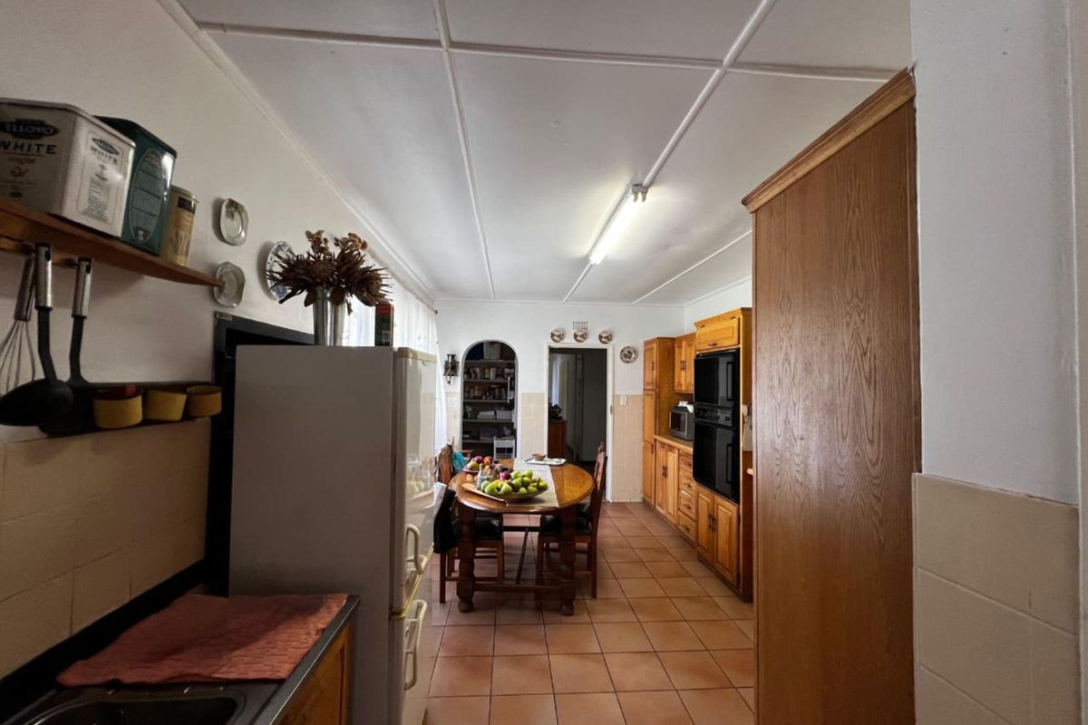 A functional kitchen and dining area featuring wooden cabinetry, built-in oven, tiled flooring, and an arched doorway leading to a scullery or pantry space.