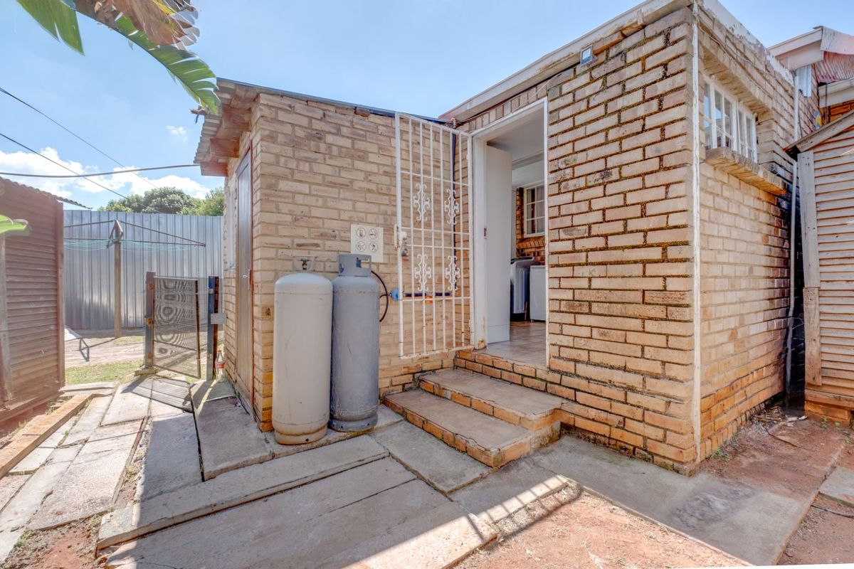 Exterior view of the rear building entrance featuring exposed brickwork, concrete steps, and a security gate.