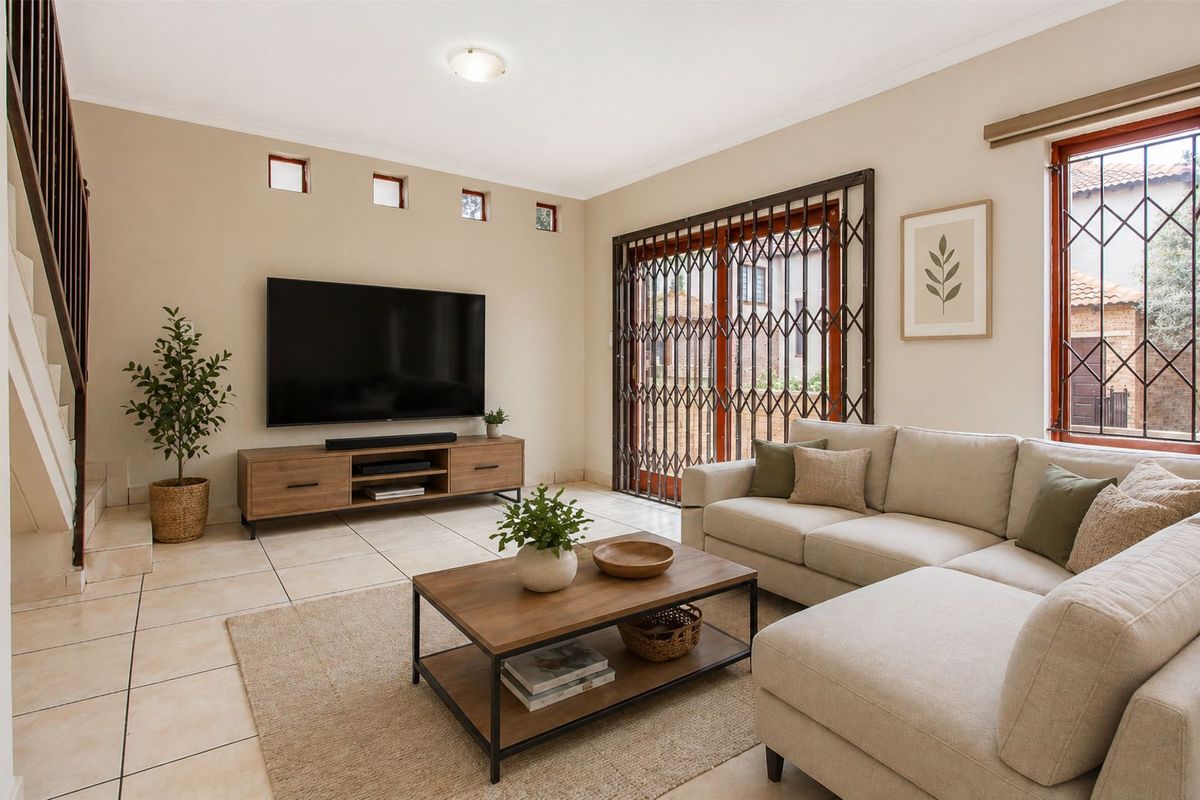 A bright and spacious living room featuring tiled flooring, a staircase, and large sliding doors secured with a metal security gate.