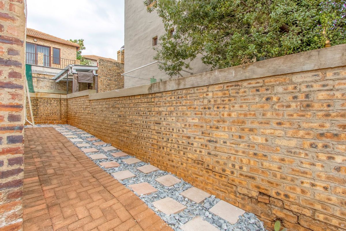 A side passage featuring brick paving, a decorative stone border with pavers, and a high face-brick boundary wall.
