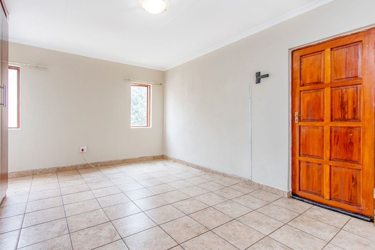 A vacant bedroom featuring neutral wall paint, tiled flooring, a wooden door, and two windows providing natural light.