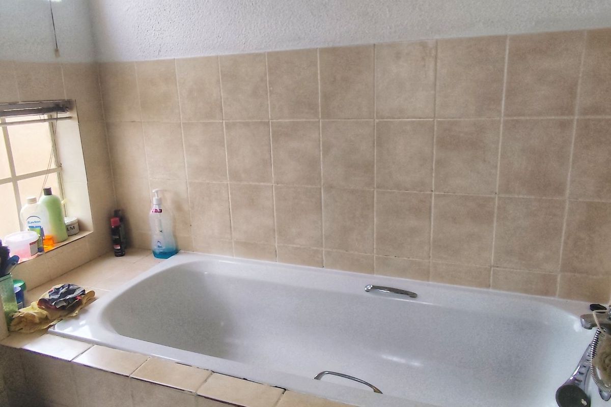 A functional bathroom featuring a built-in bathtub with tiled surround and splashback, complemented by natural light from adjacent windows.