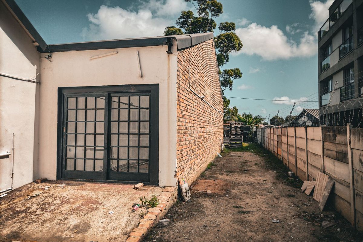 Rear exterior view of the property featuring a brick facade, sliding glass doors, and an unpaved outdoor area requiring landscaping and maintenance.