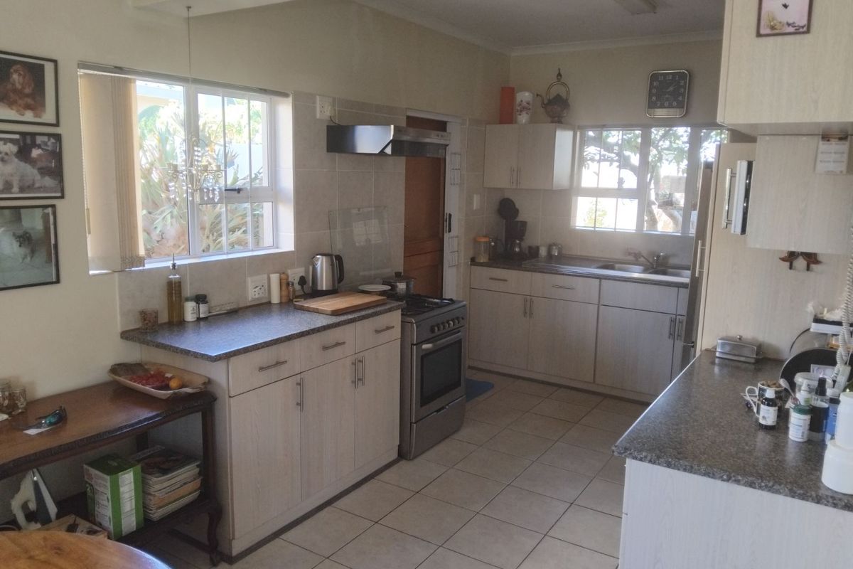 A functional kitchen featuring light-toned cabinetry, tiled flooring, a stainless steel stove with extractor fan, and ample counter space with natural light.