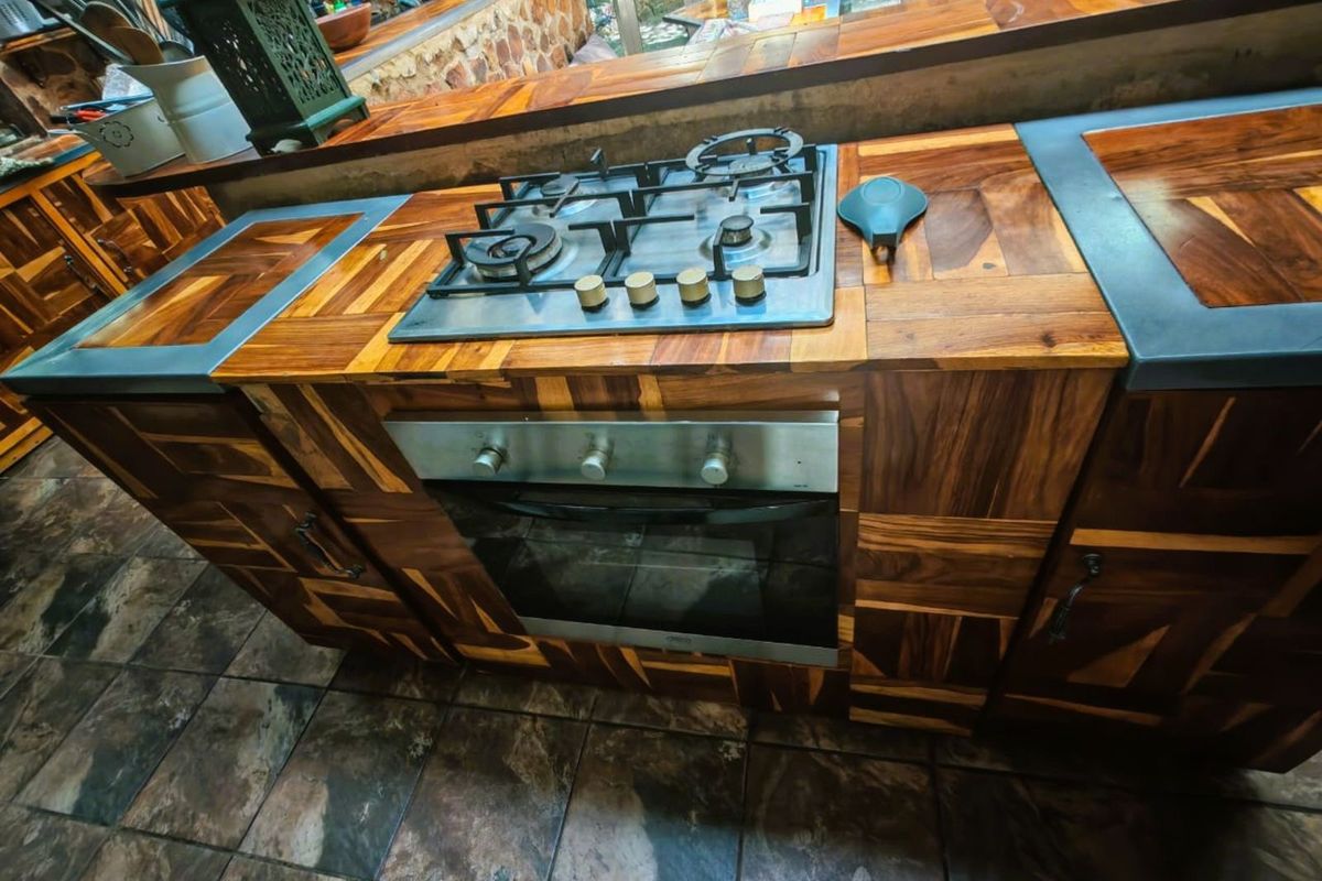 A kitchen island featuring custom wood-block cabinetry, a built-in gas hob, and an integrated oven, set against a stone-tiled floor.