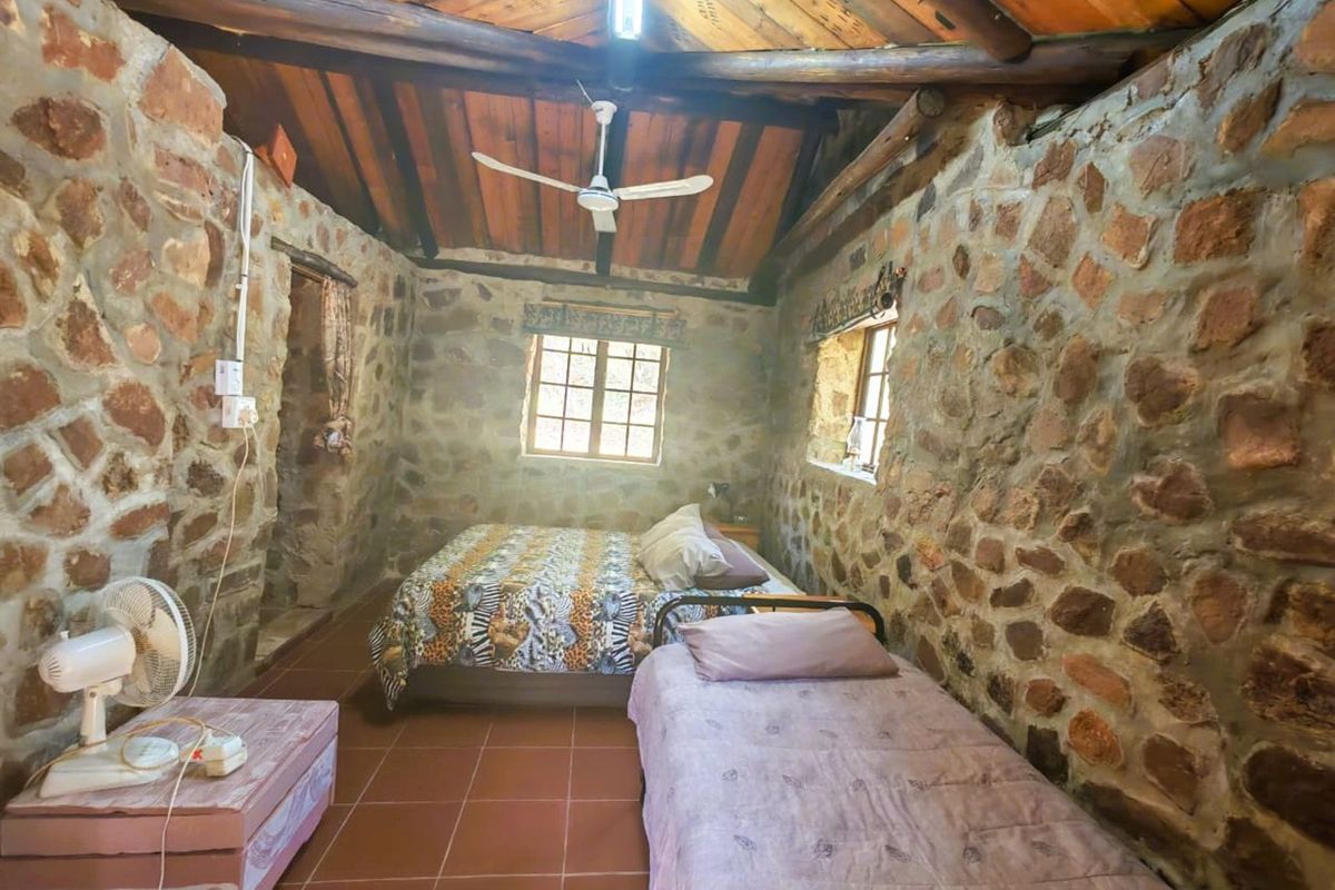 Rustic bedroom featuring exposed stone walls, timber-clad vaulted ceiling with exposed beams, tiled flooring, and natural light through multiple windows.