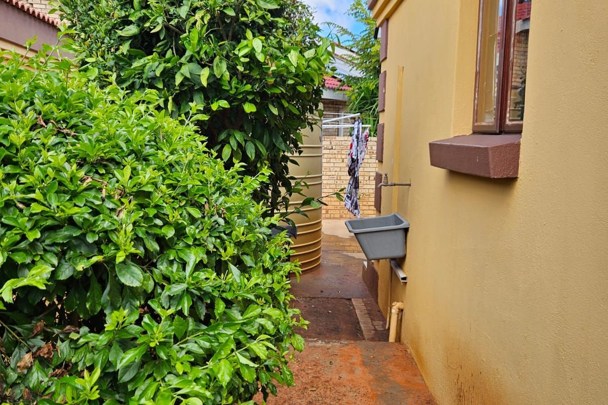 Side exterior area featuring a utility sink, water tank, and established garden shrubbery along the side of the house.
