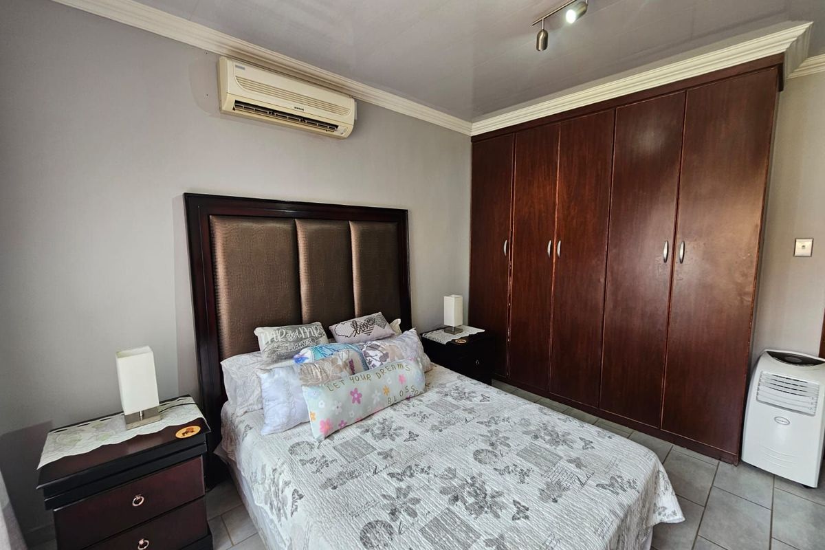 A well-maintained bedroom featuring built-in wooden cabinetry, a wall-mounted air conditioning unit, and tiled flooring.