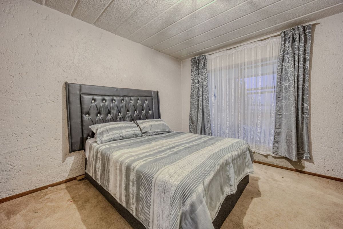 A bedroom featuring textured walls, a textured ceiling, and carpet flooring, with a large window providing natural light.