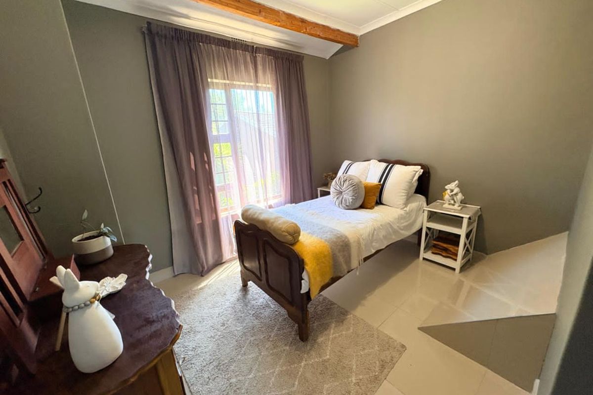 A cozy bedroom featuring tiled flooring, a decorative exposed ceiling beam, and a sliding glass door providing natural light.