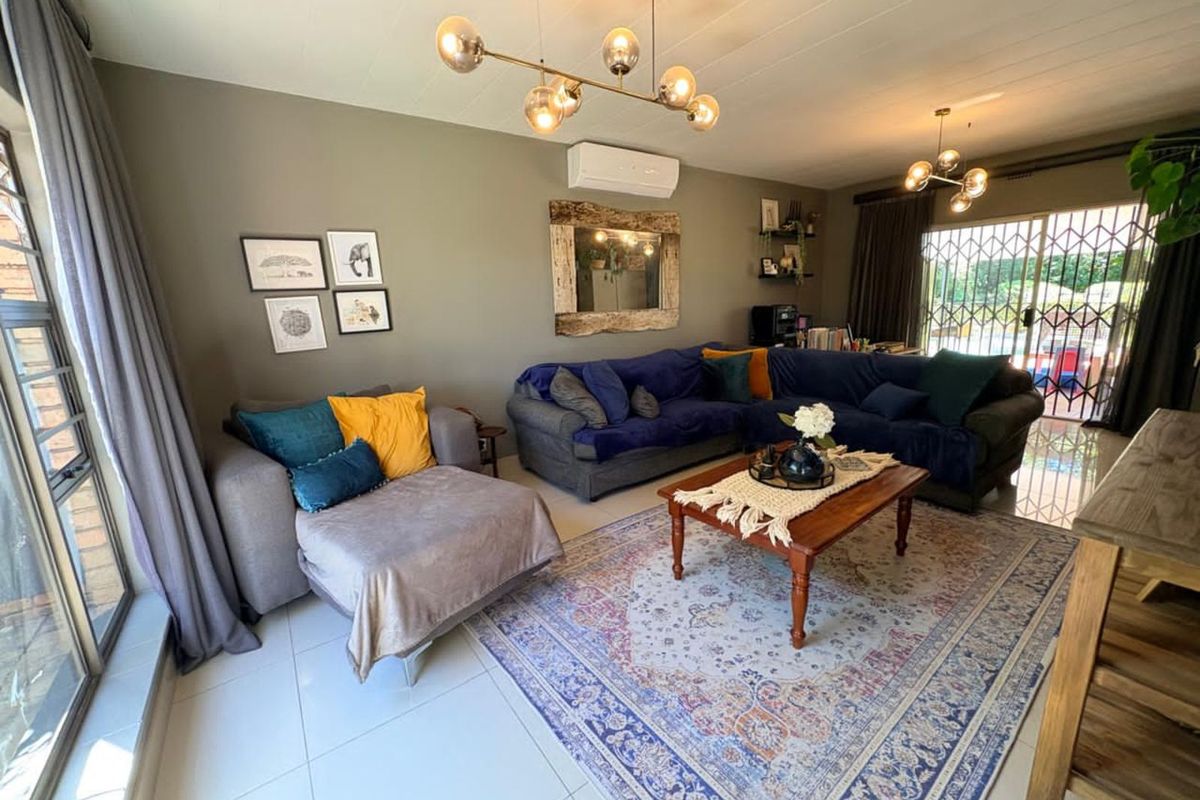 Spacious living room featuring tiled flooring, modern multi-bulb pendant lighting, and a wall-mounted air conditioning unit with access to the patio.