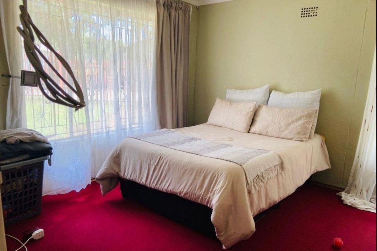 A bedroom featuring red carpeting and neutral wall tones, with large windows allowing natural light into the space.