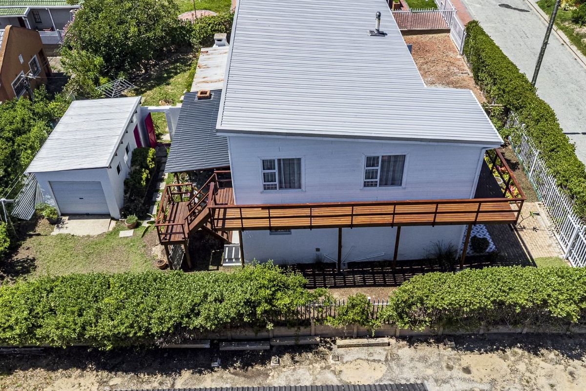 Aerial view of a detached house featuring a corrugated metal roof, elevated timber deck, and a separate garage structure set within a landscaped garden.