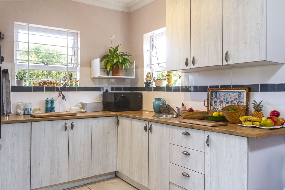 A functional kitchen featuring light wood-grain cabinetry, timber-look countertops, tiled splashbacks, and dual windows providing natural light.