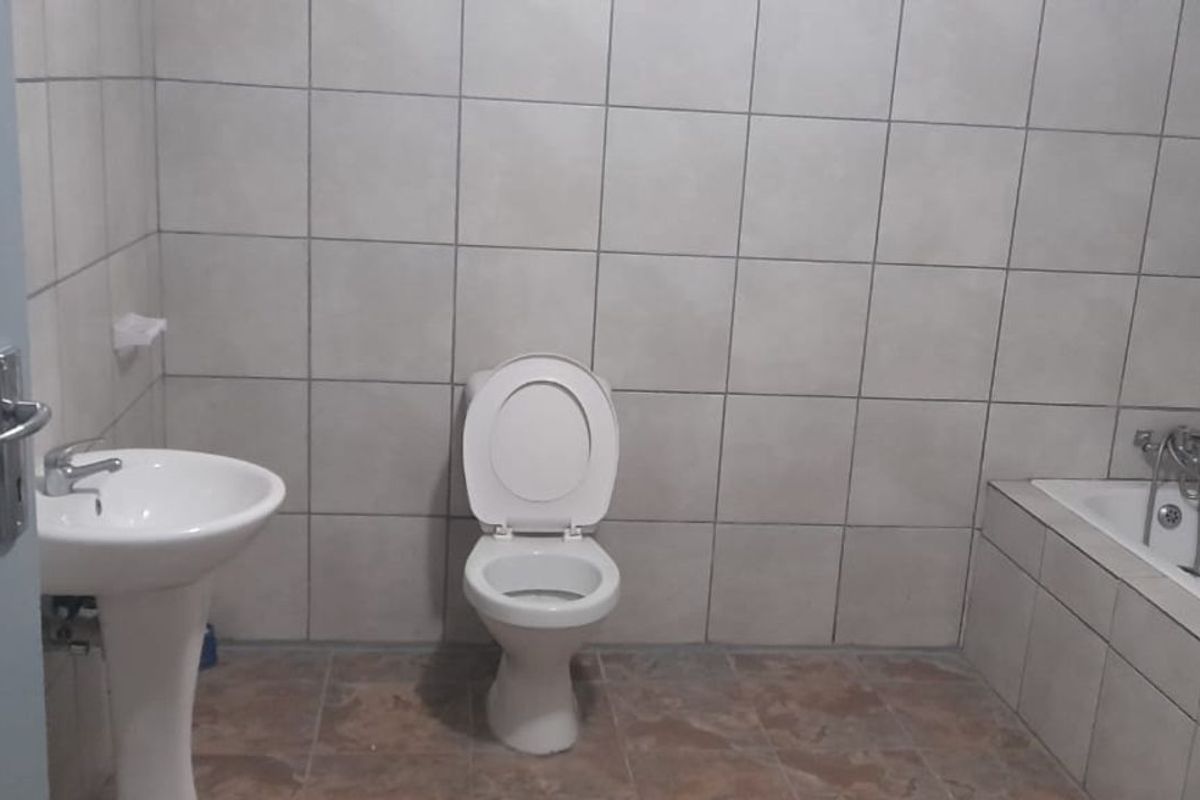 A functional bathroom featuring a pedestal basin, a standard toilet, and a built-in bathtub with wall-to-wall tiling.